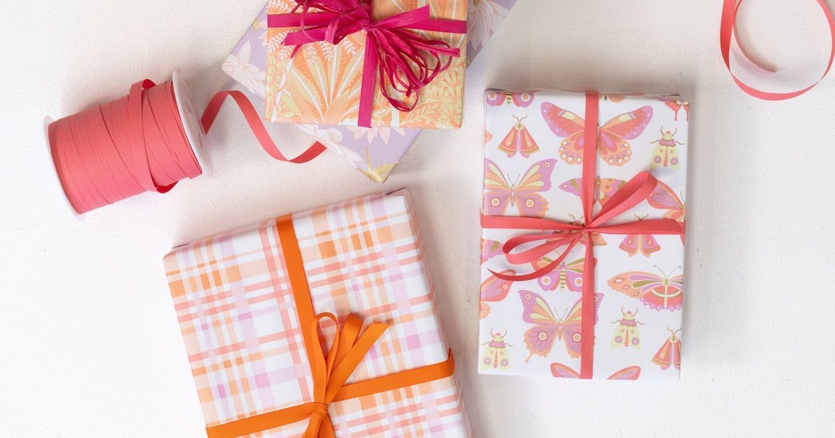 Four types of wraps from the 2024 Everyday Wrap range featuring vibrant, girly designs: hot pink, yellow, and orange wraps with gingham, butterfly, and floral patterns, each paired with orange ribbons.