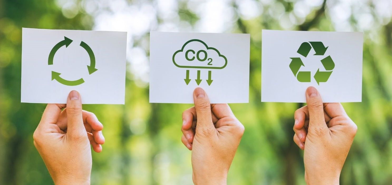 Three hands holding pieces of paper depicting carbon management concepts: one with a circular arrow symbol, one with ‘CO2’ and a cloud with downward arrows, and one with a recycling symbol, representing Bee Dee Bags' commitment to sustainability.